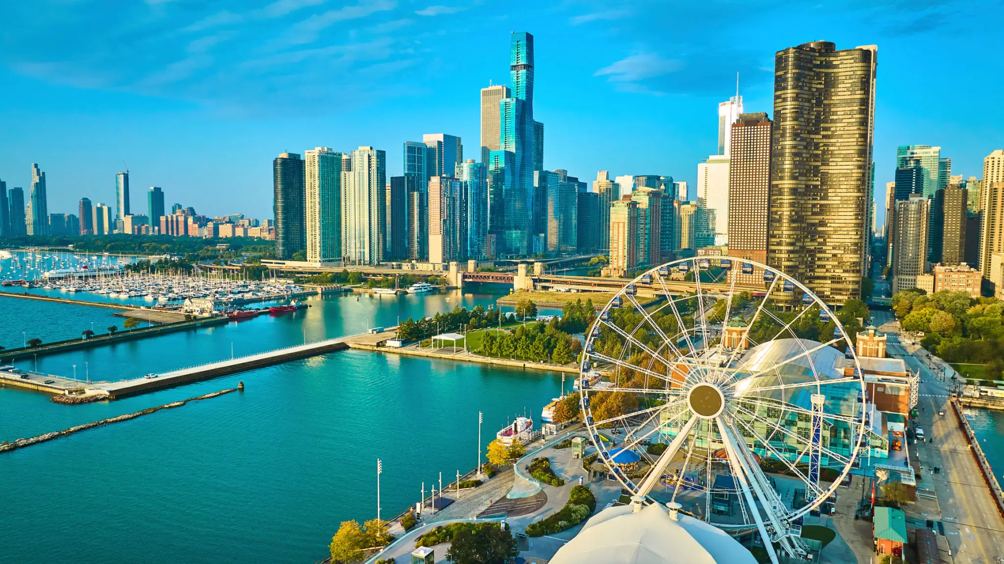 City skyline with a Ferris wheel by the waterfront under a bright blue sky.