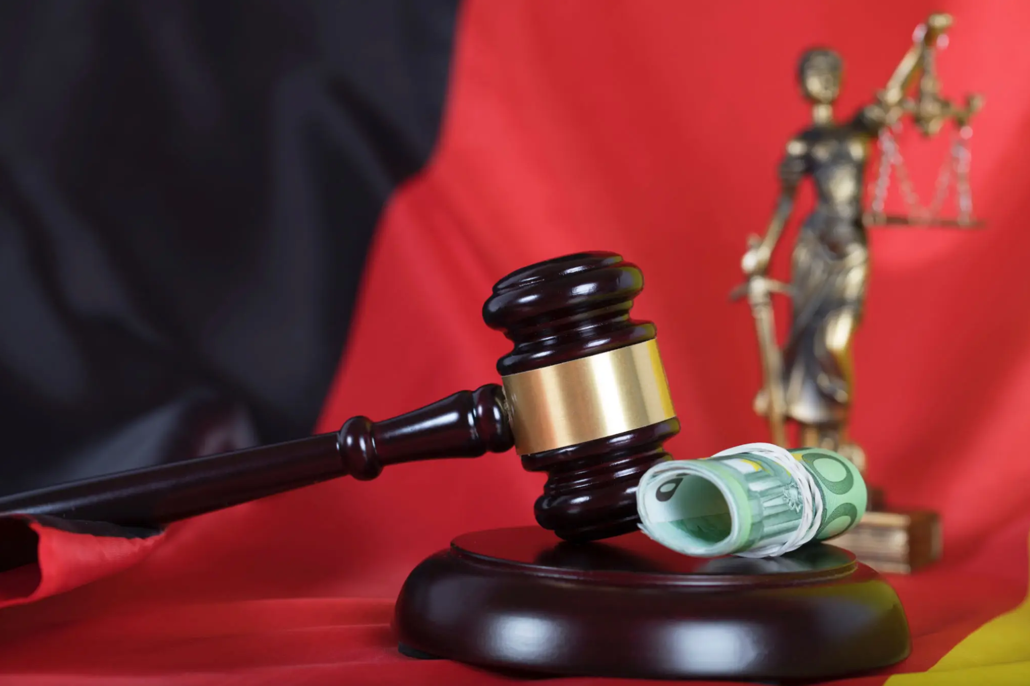 Judge's gavel, money, and Lady Justice statue on red background.