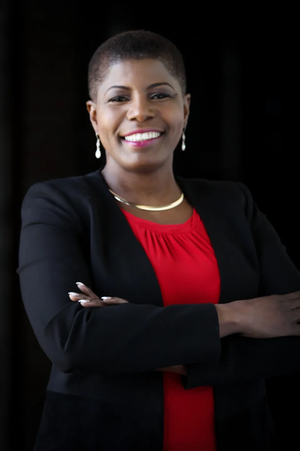 Confident professional woman in business attire smiling with arms crossed.